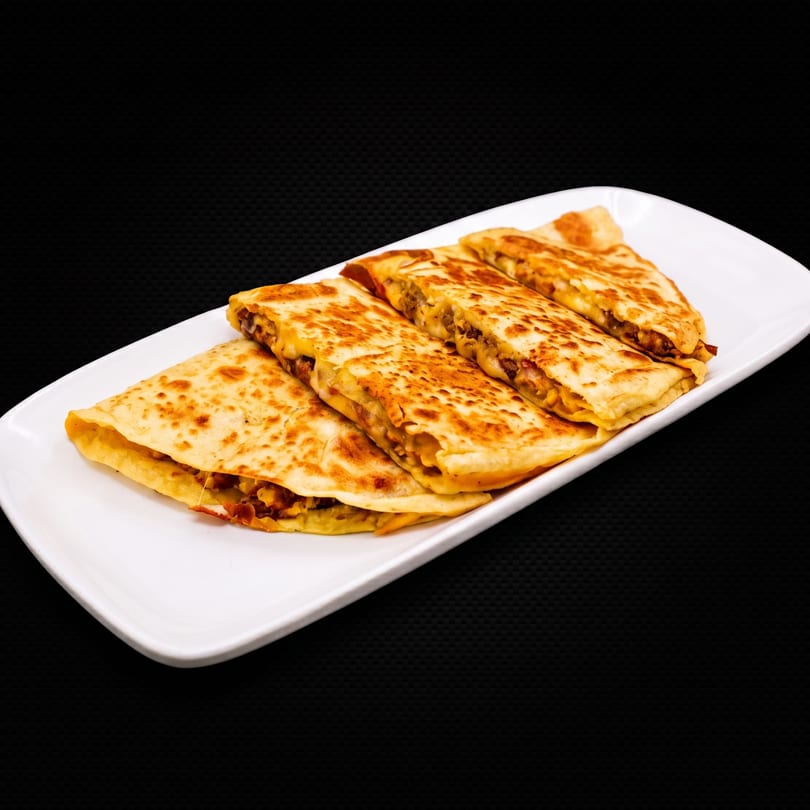 A white rectangular plate holds four golden-brown quesadillas filled with meat and melted cheese.